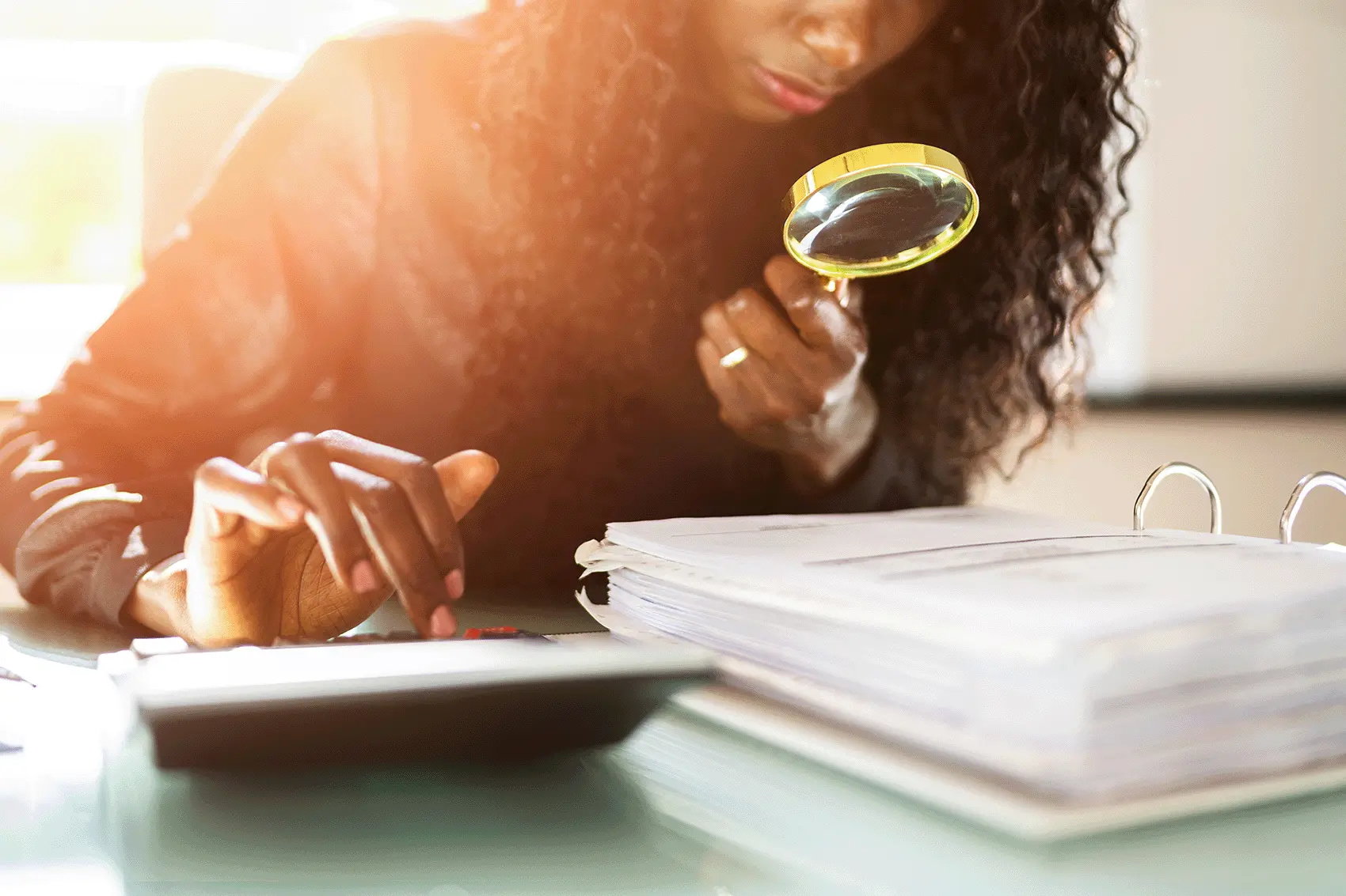 Person with magnifying glass and calculator studying information in a large ringbinder file as part of a HSS Training auditing course
